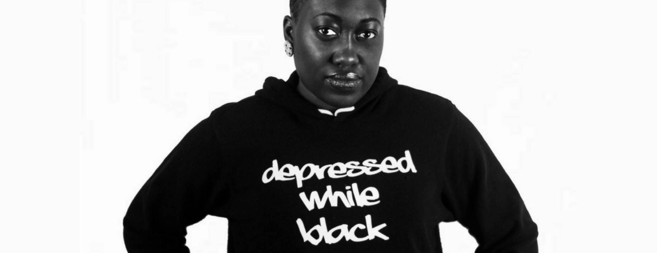 Imadé Nibokun (she/her), an individual living with depression wearing a hoodie with the words "depressed while black"